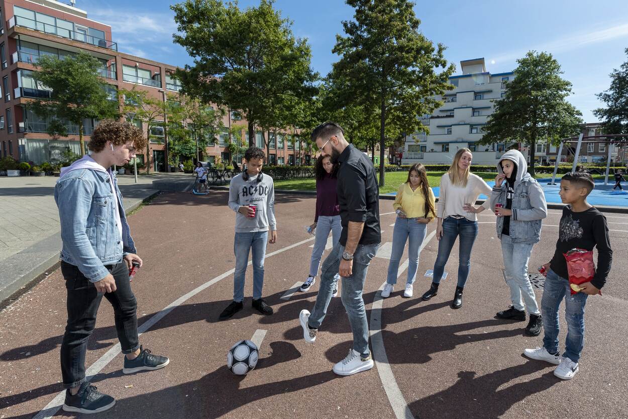 Een groep jongeren is aan het spelen op een plein in een wijk met sociale huurwoningen